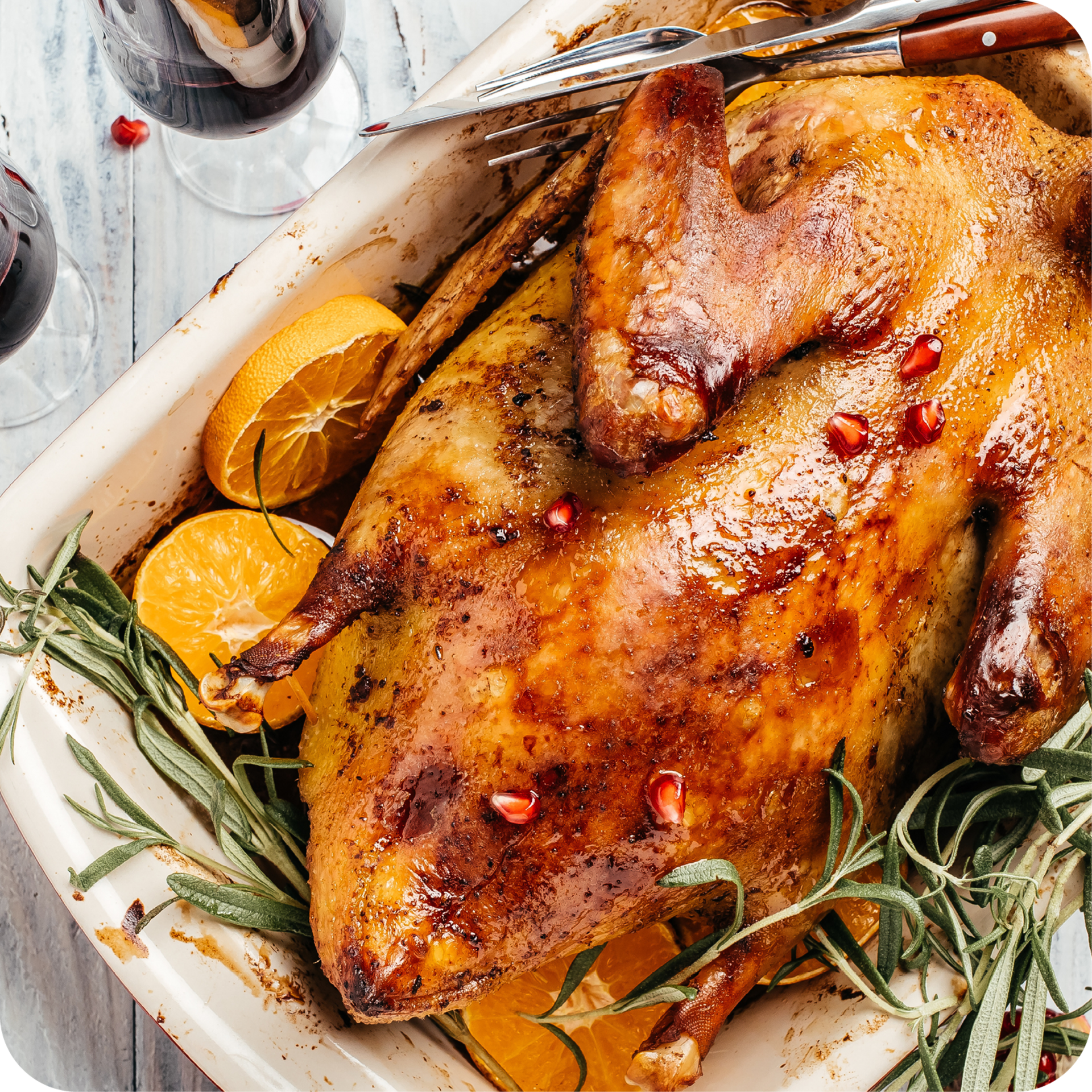 Ganze gebratene Gans auf Teller, umgeben von gebratenem Gemüse und Rosmarinzweigen.