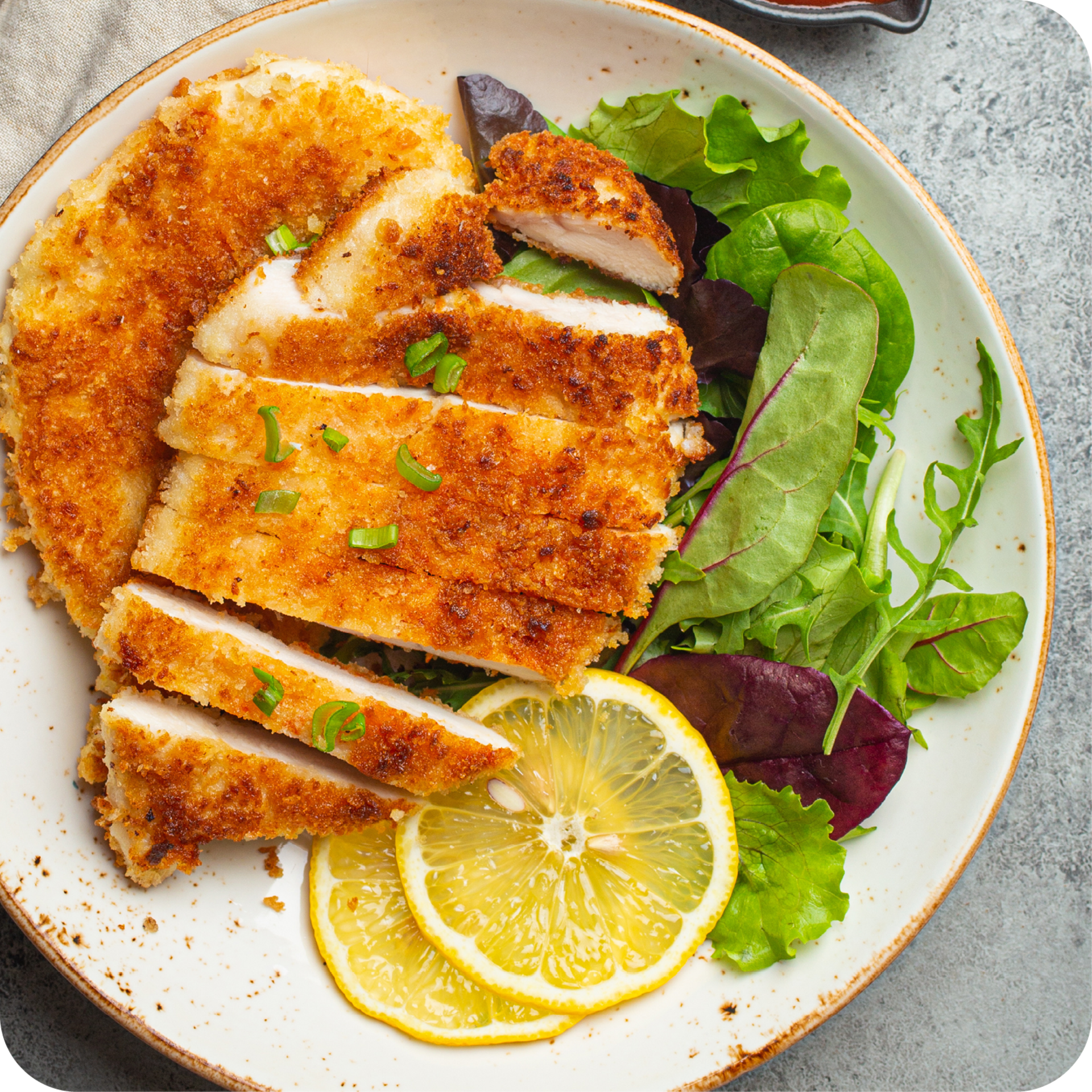 Panierte Schnitzel auf weißem Teller mit grünem Salat und kleinem Becher Sauce